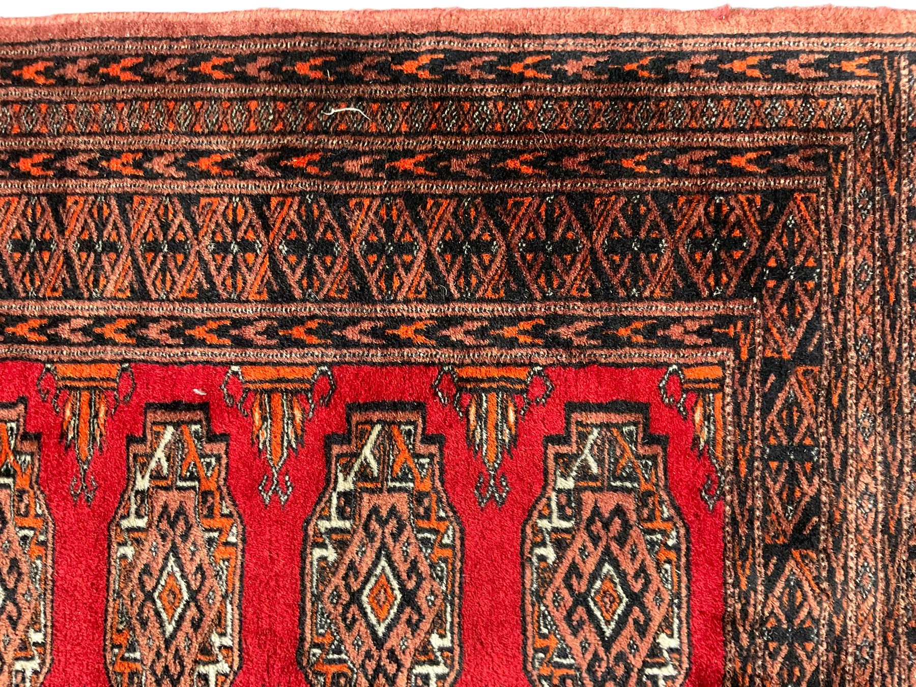 Persian Bokhara dark amber round rug, crimson field with six Gul motifs, surrounded by a guarded border with geometric design (124cm x 70cm); together with another similar in amber and red (101cm x 63cm) (2)