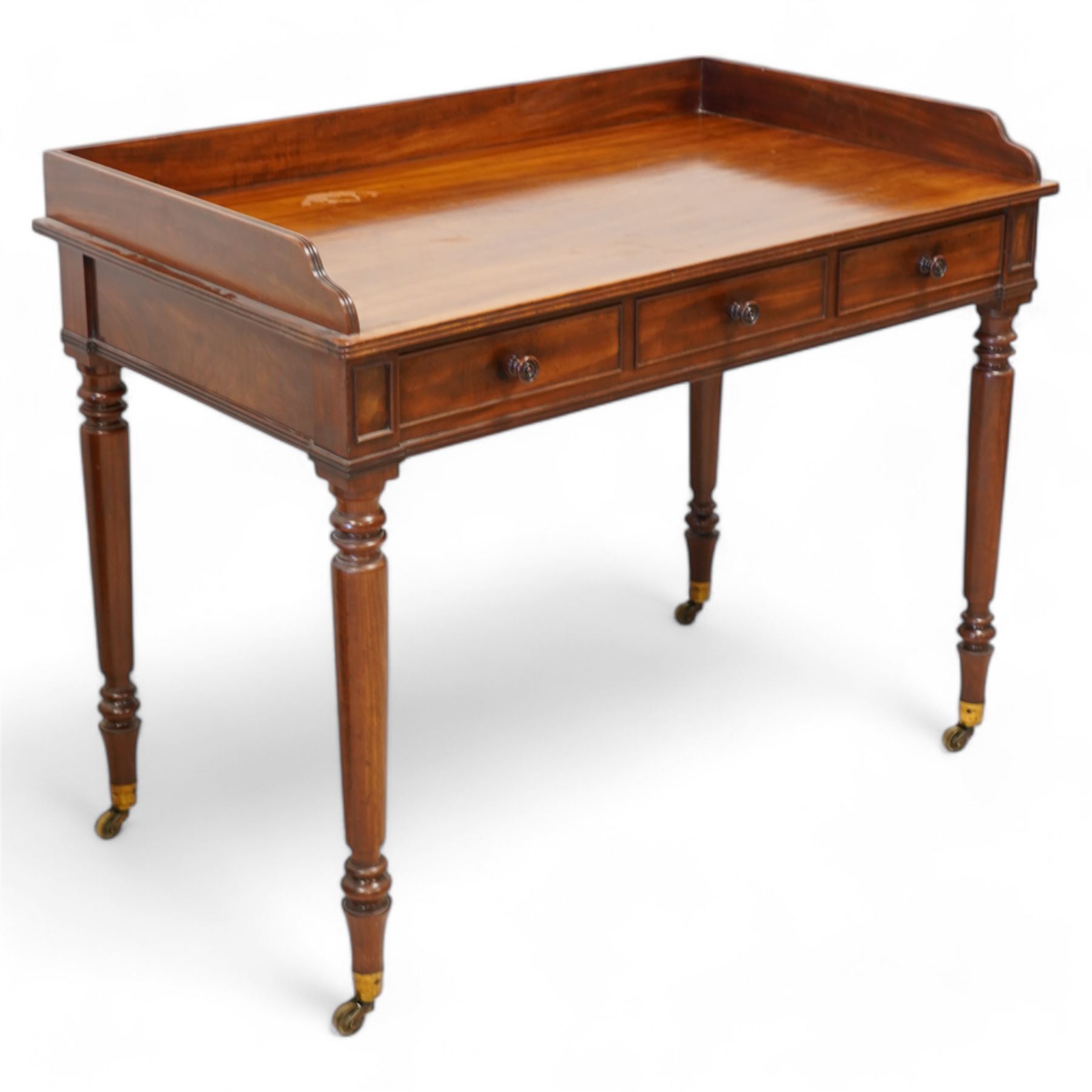 Gillows, Lancaster - early 19th century mahogany writing table, reeded three-quarter gallery over rectangular top with reed moulded edge, fitted with three cocked-beaded drawers with turned handles, the central drawer stamped 'Gillows Lancaster'. on turned supports with brass cups and castors 