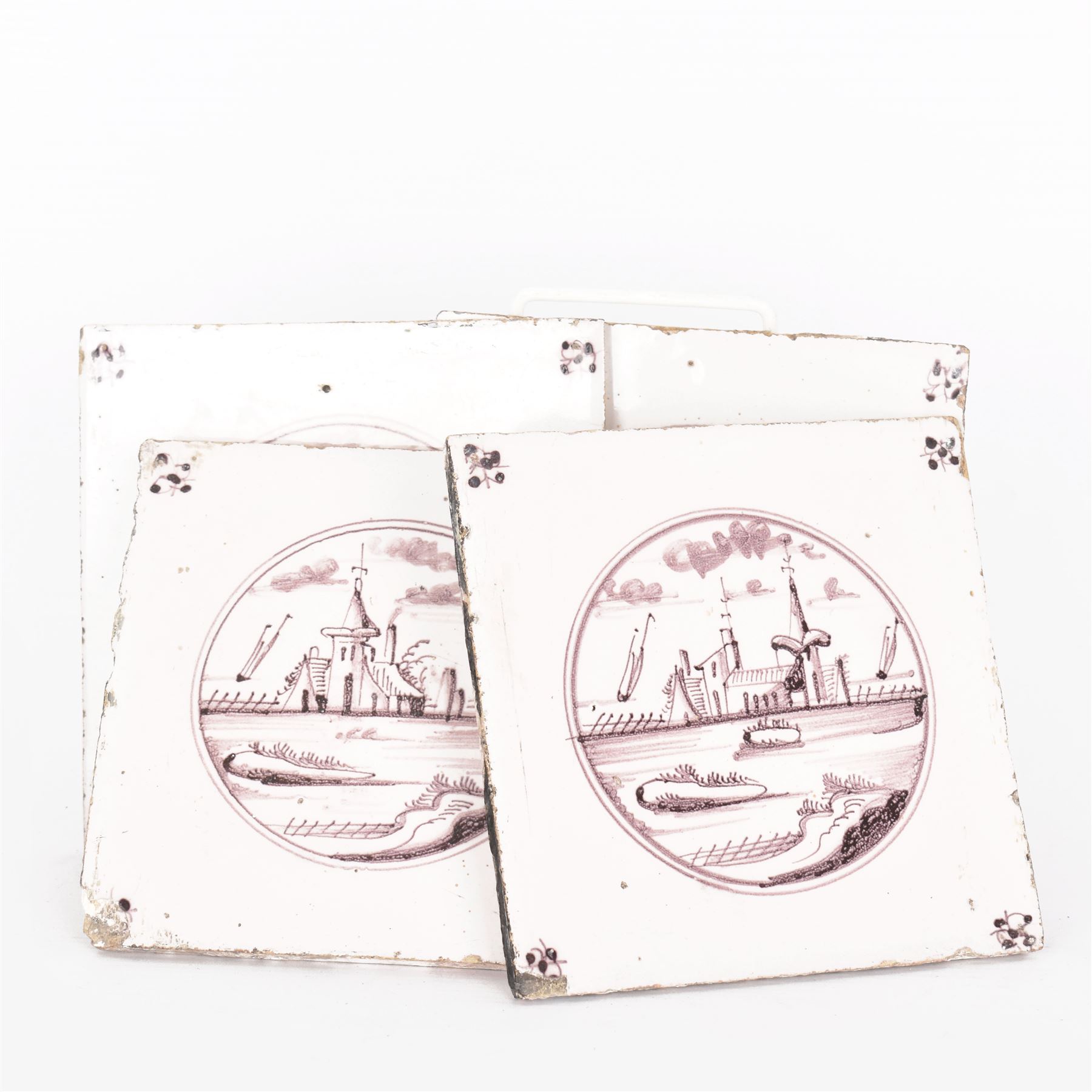 Four Dutch Delft manganese tiles, each depicting a river scene to the centre with a flower to each corner, each tile 12.5cm x 12.5cm