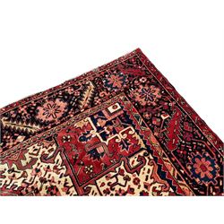 Persian Heriz red ground carpet, large central eight point medallion with projecting palmettes surrounded by small geometric motifs, decorated profusely with hooks, rosettes and animals, the busy border decorated with stylised foliate motifs within guard stripes 