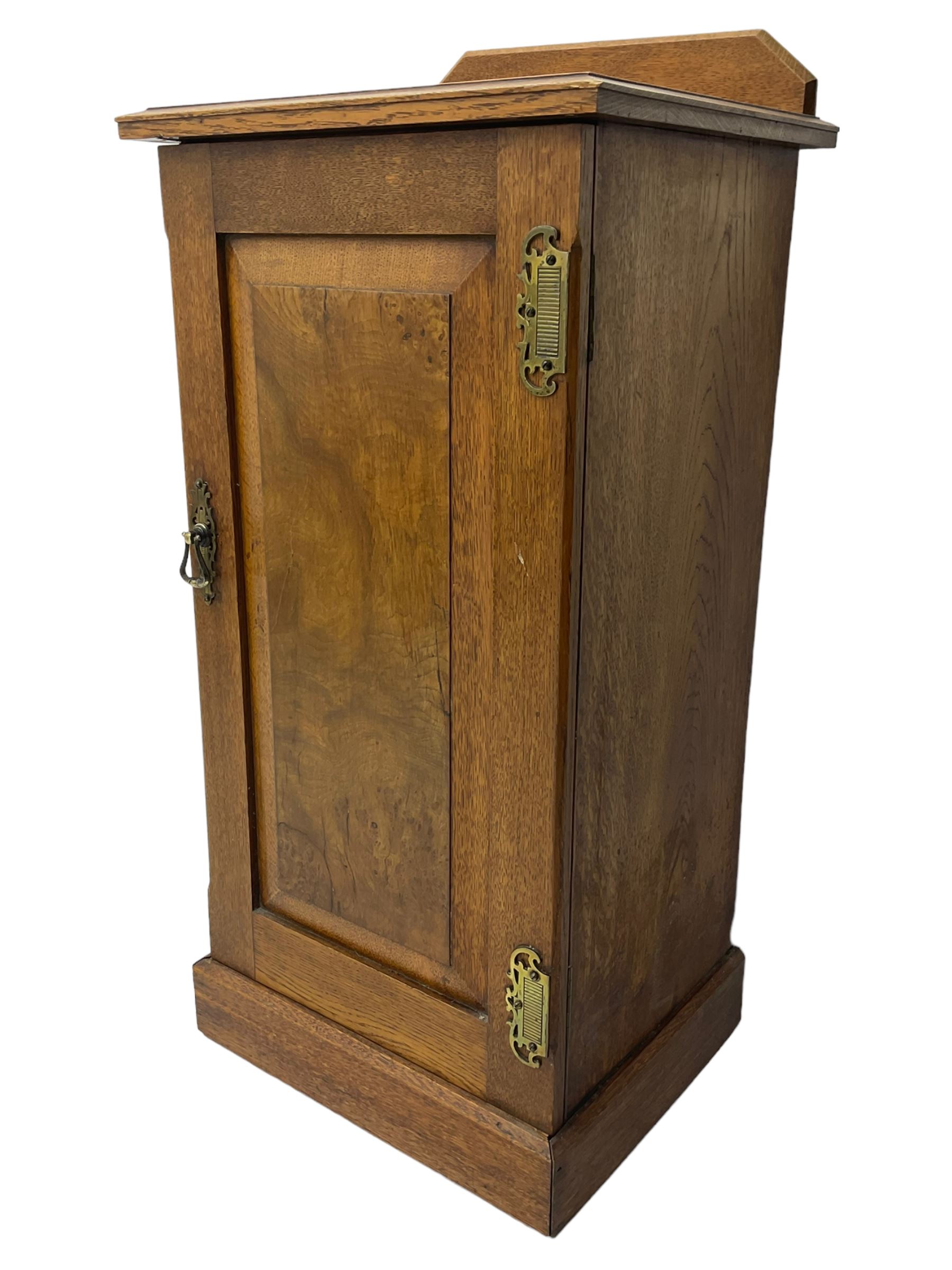 Edwardian oak bedside cabinet, raised back over moulded top, enclosed by panelled door, the interior fitted with shelves, on chamfered plinth base 