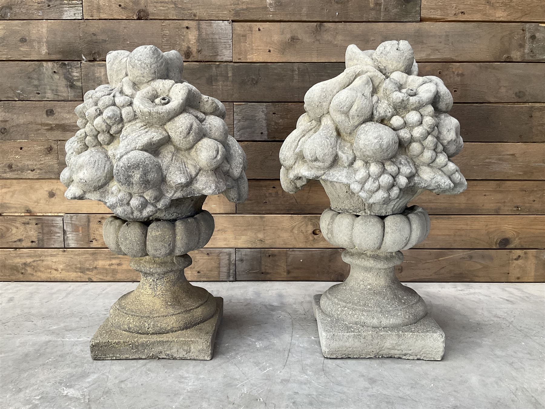 Pair of cast stone garden wall or gate finials depicting Fruit Piers, raised on separate circular squat column with plinth base