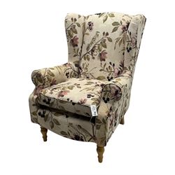 Hardwood-framed wingback armchair, upholstered in cream floral pattern fabric, on turned front feet