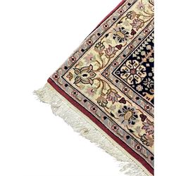 Persian design crimson ground rug, the field decorated with tree of life and floral motifs, enclosed by indigo spandrels with stylised flower head decoration, repeating scrolling border 