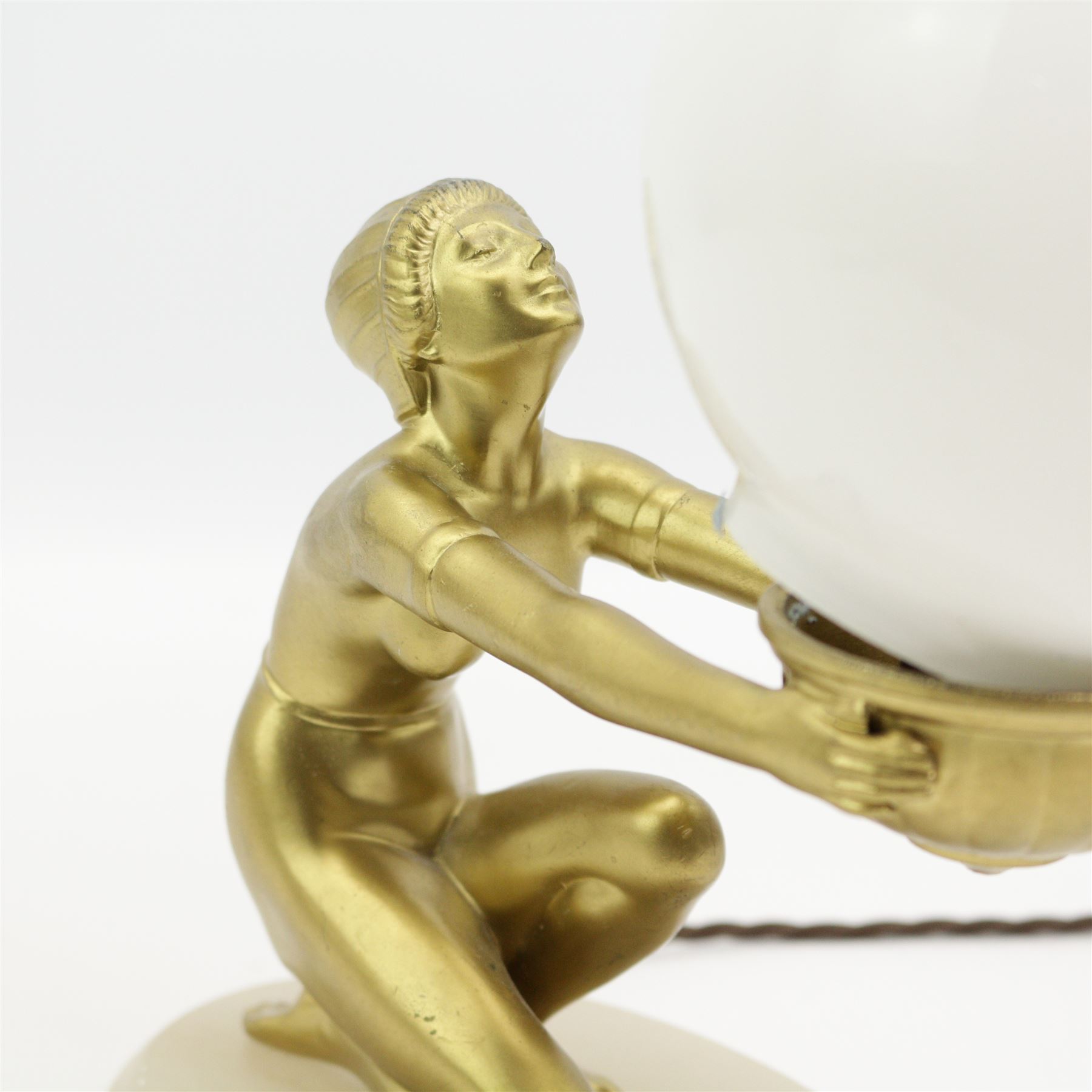 Art Deco gilt patinated spelter table lamp, modelled as a semi-nude female, kneeling with arms outstretched and holding the globular opaque glass shade, mounted upon an oval alabaster plinth, H27cm 