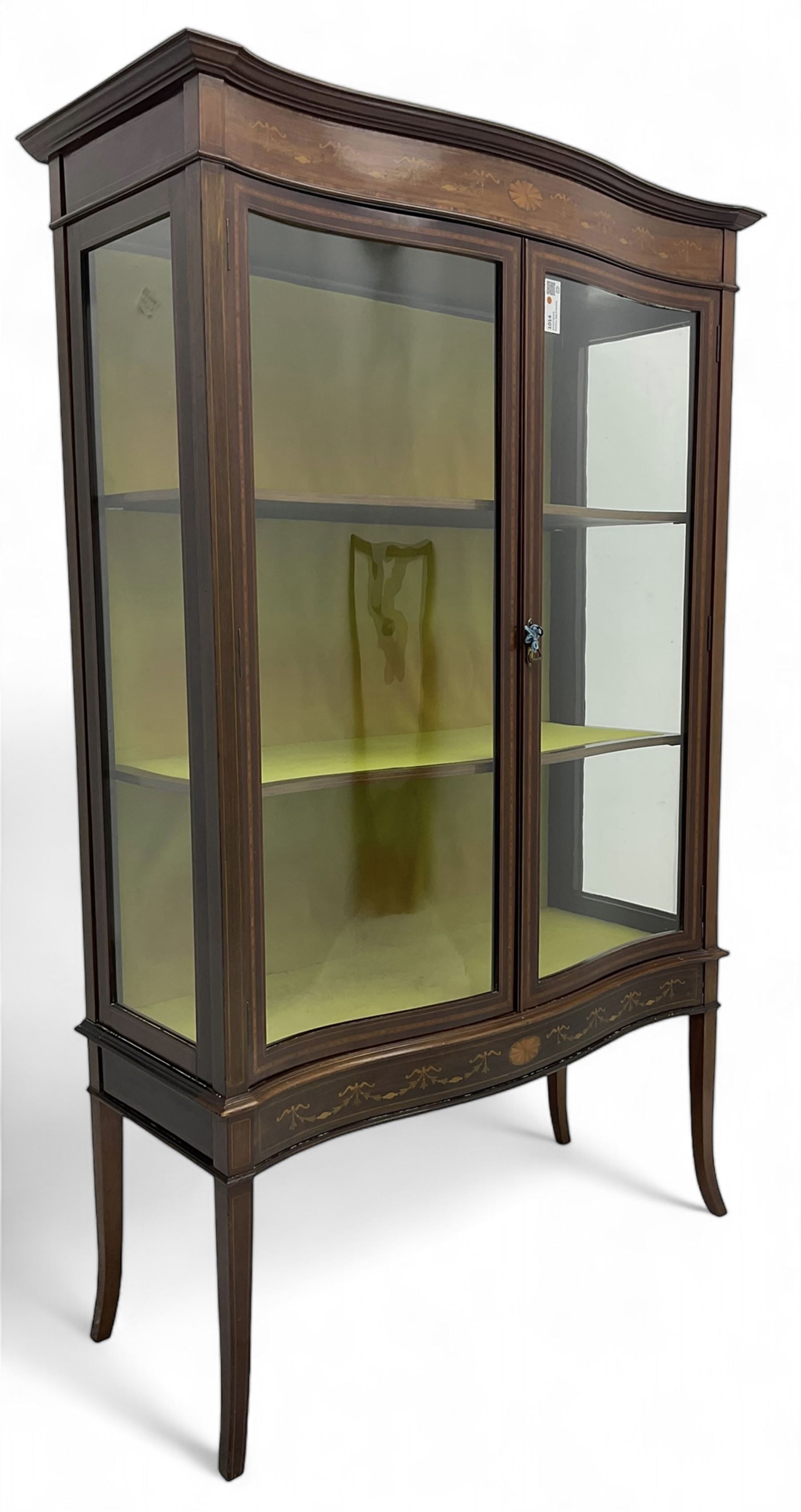 Edwardian inlaid mahogany serpentine display cabinet, projecting moulded cornice over figured frieze inlaid with tailing bellflowers and central fan motif, enclosed by two glazed doors, on square tapering supports with splayed terminals 