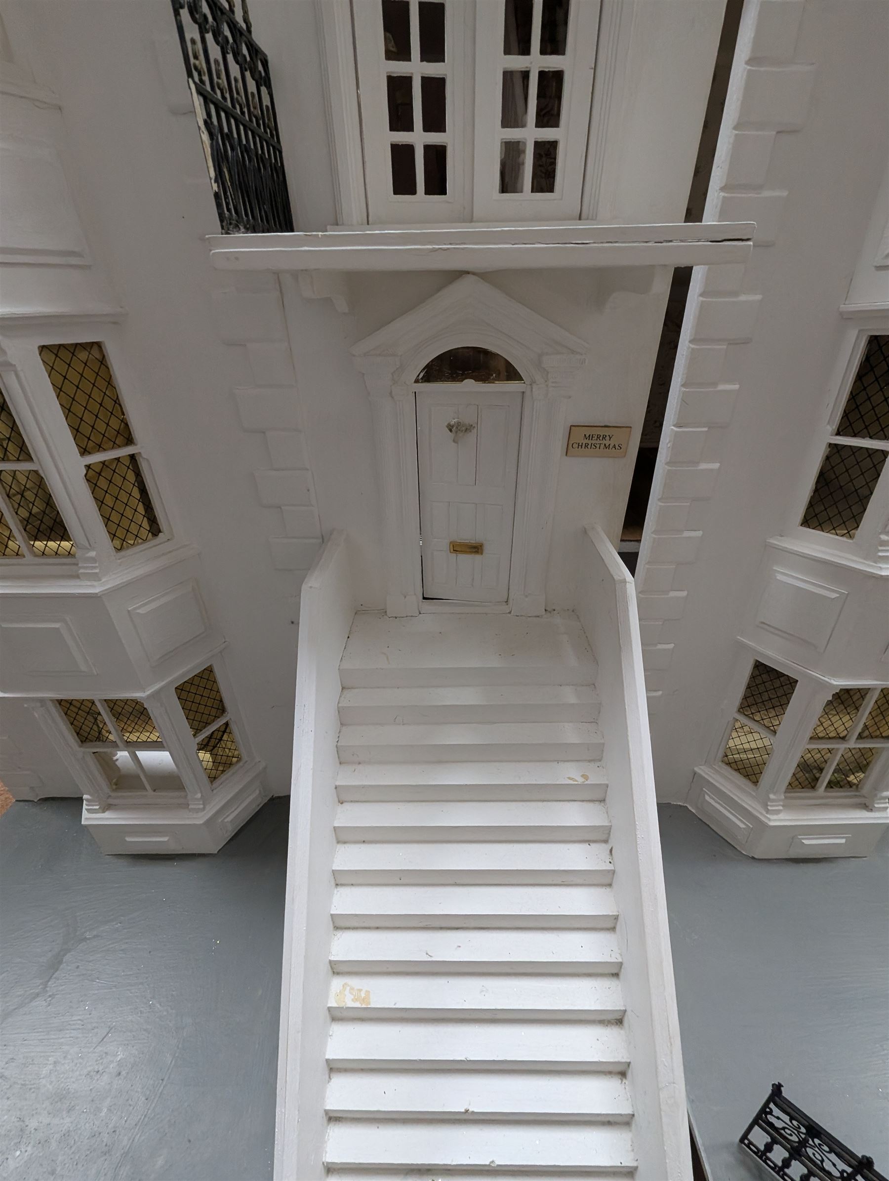 Large three storey modern dolls house, painted white with latticed windows, grey roof and metal fencing, with decorated interior, together with two dolls house garden rooms and two conservatories