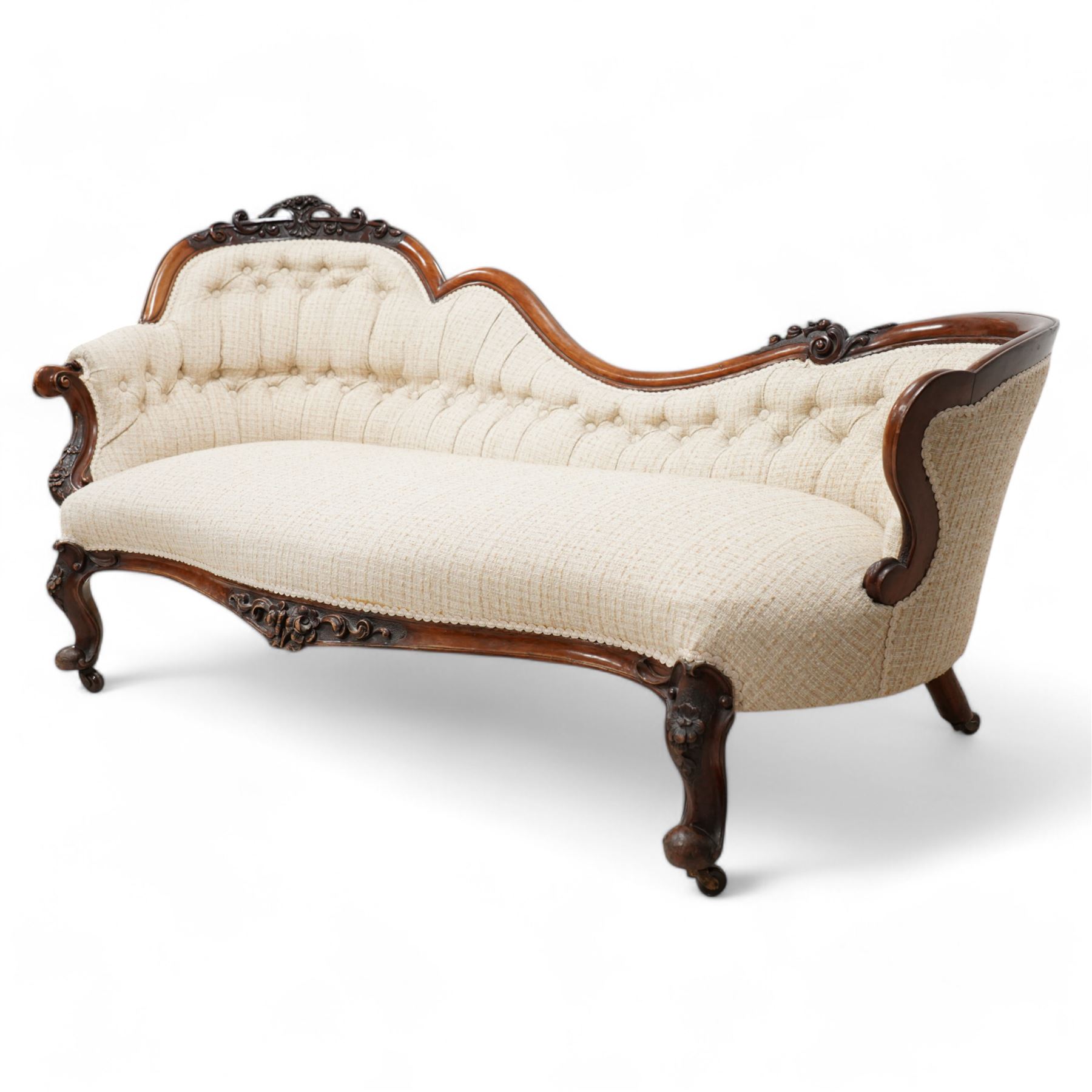 Victorian walnut framed chaise longue, the shaped frame carved with scrolls and flower heads, upholstered in buttoned textured cream fabric, the shaped seat rail carved with flower heads and extending foliate scrolls, on floral carved cabriole feet with castors 