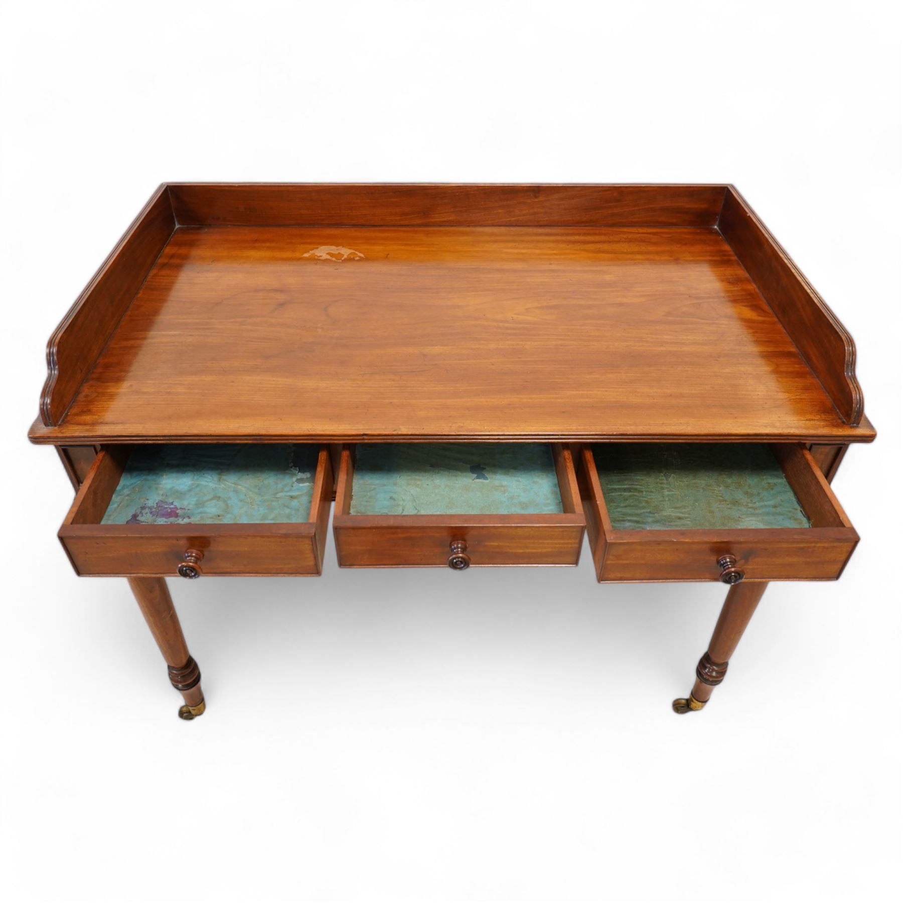 Gillows, Lancaster - early 19th century mahogany writing table, reeded three-quarter gallery over rectangular top with reed moulded edge, fitted with three cocked-beaded drawers with turned handles, the central drawer stamped 'Gillows Lancaster'. on turned supports with brass cups and castors 