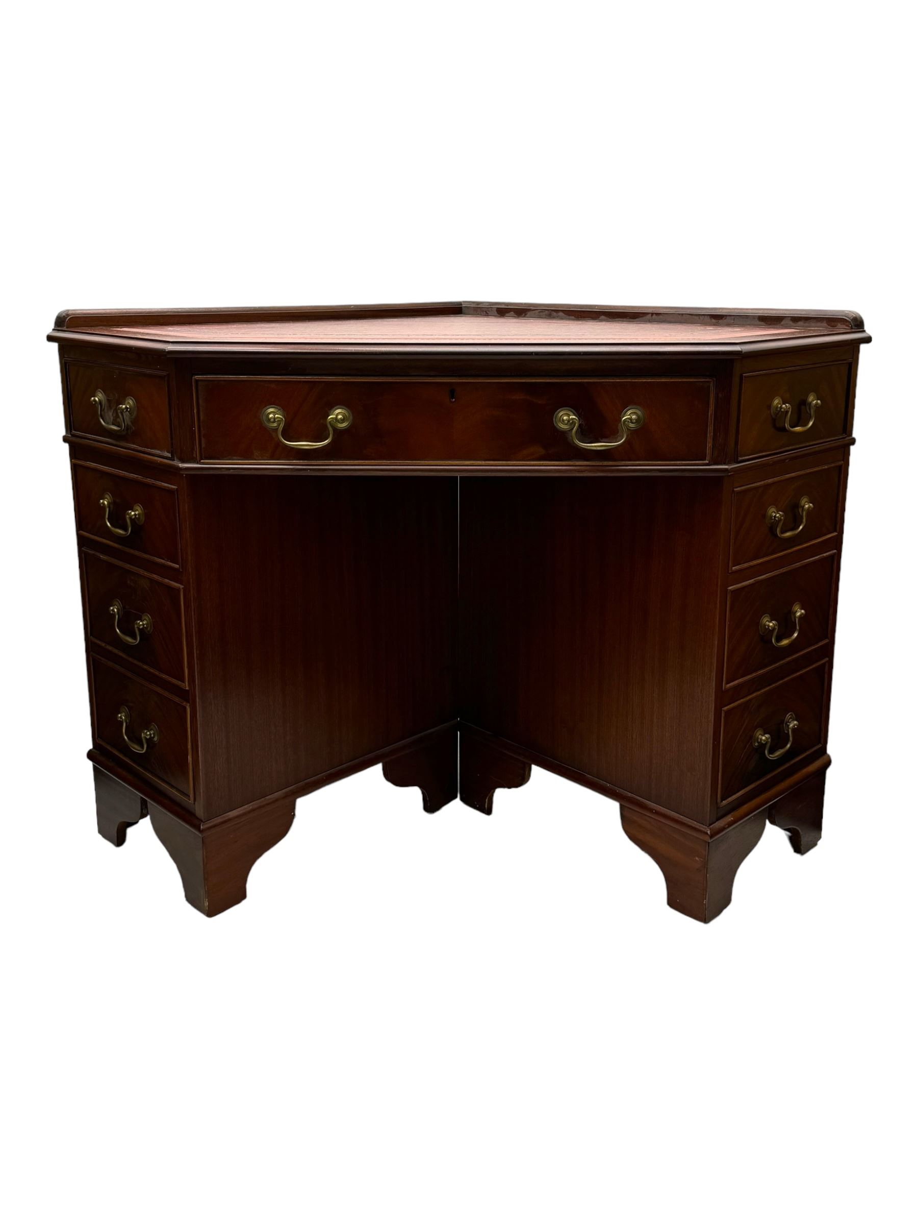 Late 20th century mahogany corner desk, leather inlaid top with gilt tooling, central frieze drawer flanked by two banks of four graduated drawers, raised on shaped bracket supports 