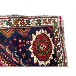 Persian Quashqai crimson ground rug, central geometric lozenge medallion surrounded by stylised plant motifs, indigo spandrels with further geometric designs, enclosed by an ivory border