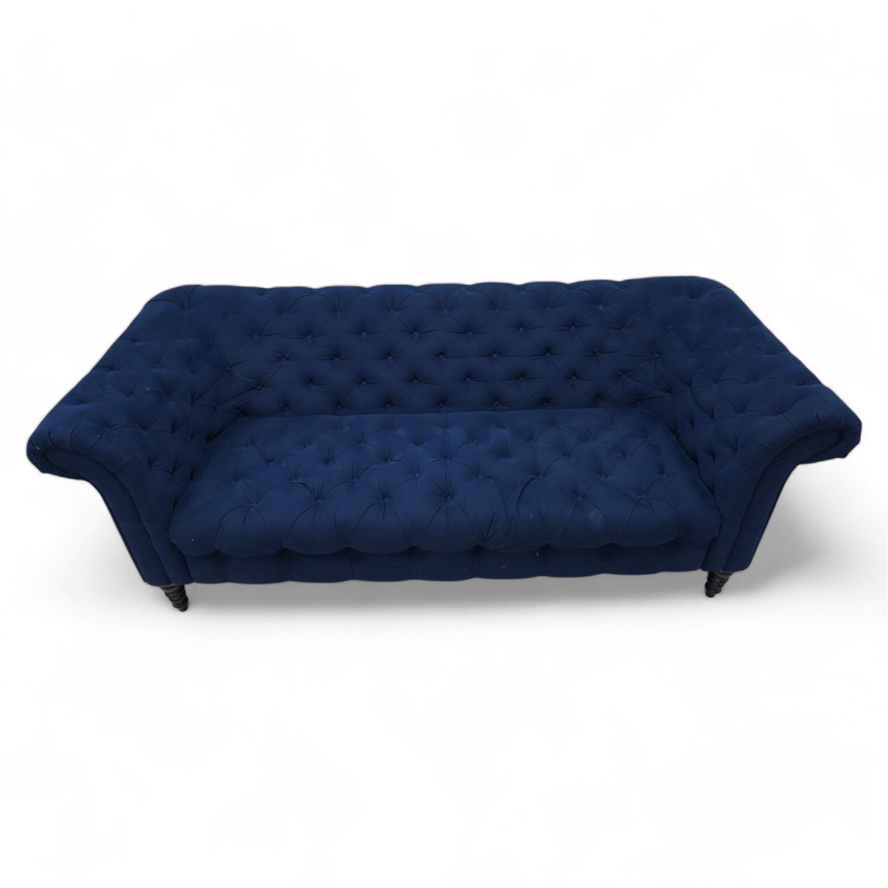 Chesterfield three-seat sofa, traditional shape with rolled arms, upholstered in deep blue buttoned fabric, on black finish turned front feet 