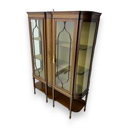 Edwardian inlaid mahogany display cabinet, projecting moulded cornice over two glazed doors, flanked by curved glazed sides and central arched panel with floral medallion, raised on square tapering supports with spade feet united by undertier