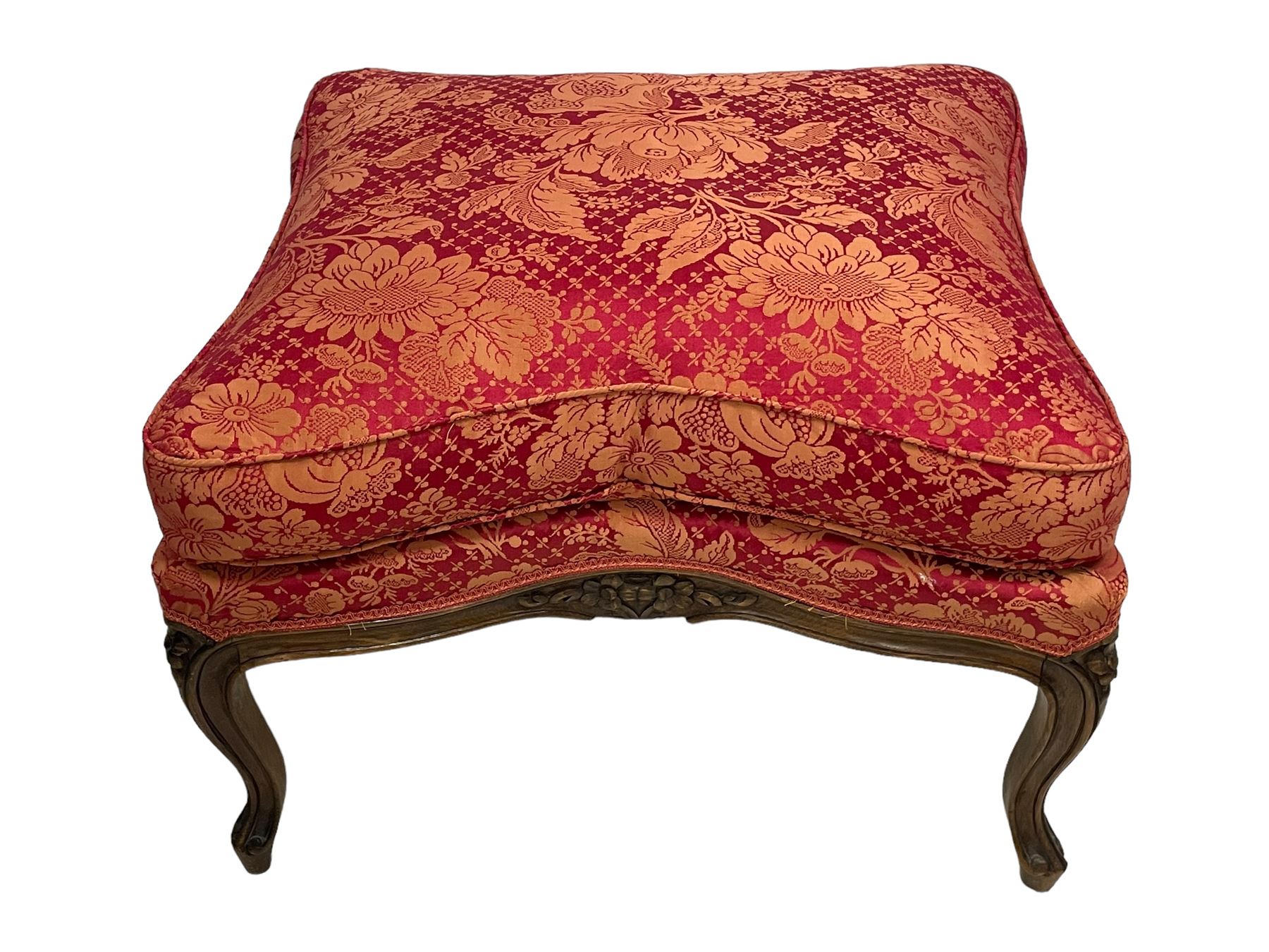 Late 20th century French design stained beech framed armchair and matching stool - the armchair with shaped and moulded frame carved with flower heads and foliage, upholstered in silk red and gold ground fabric with floral pattern, on scroll carved cabriole feet decorated with flower head carvings (W73cm, H82cm, D75cm); the footstool of concaved rectangular form with moulded frame carved with flower heads, upholstered loose cushion, on cabriole feet (70cm x 64cm, H48cm)