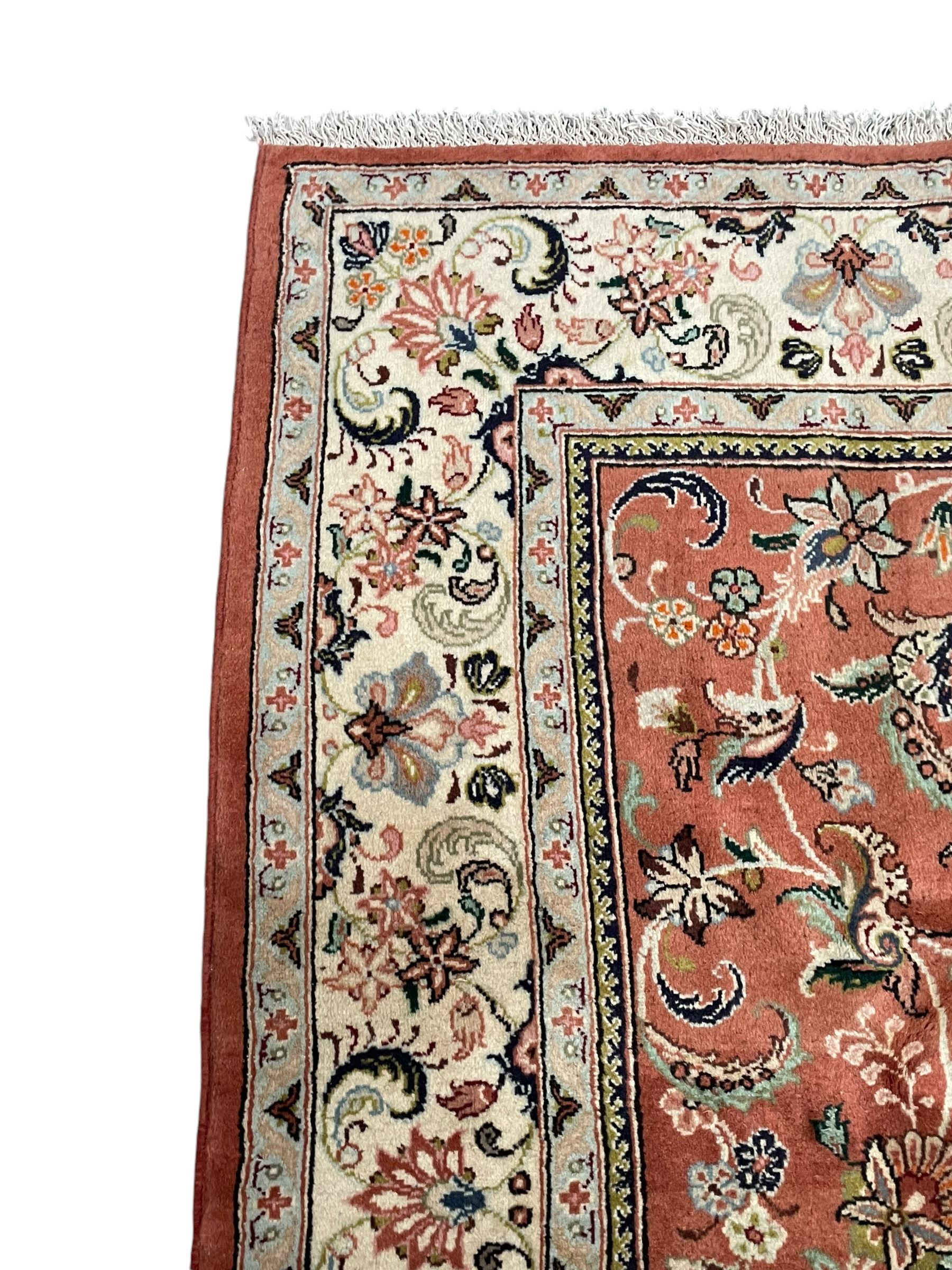 Persian Kashan peach ground rug, the field decorated with swirling leafy branches and stylised plant motifs, ivory ground border with trailing foliate design interspersed with flower heads, within guard stripes 