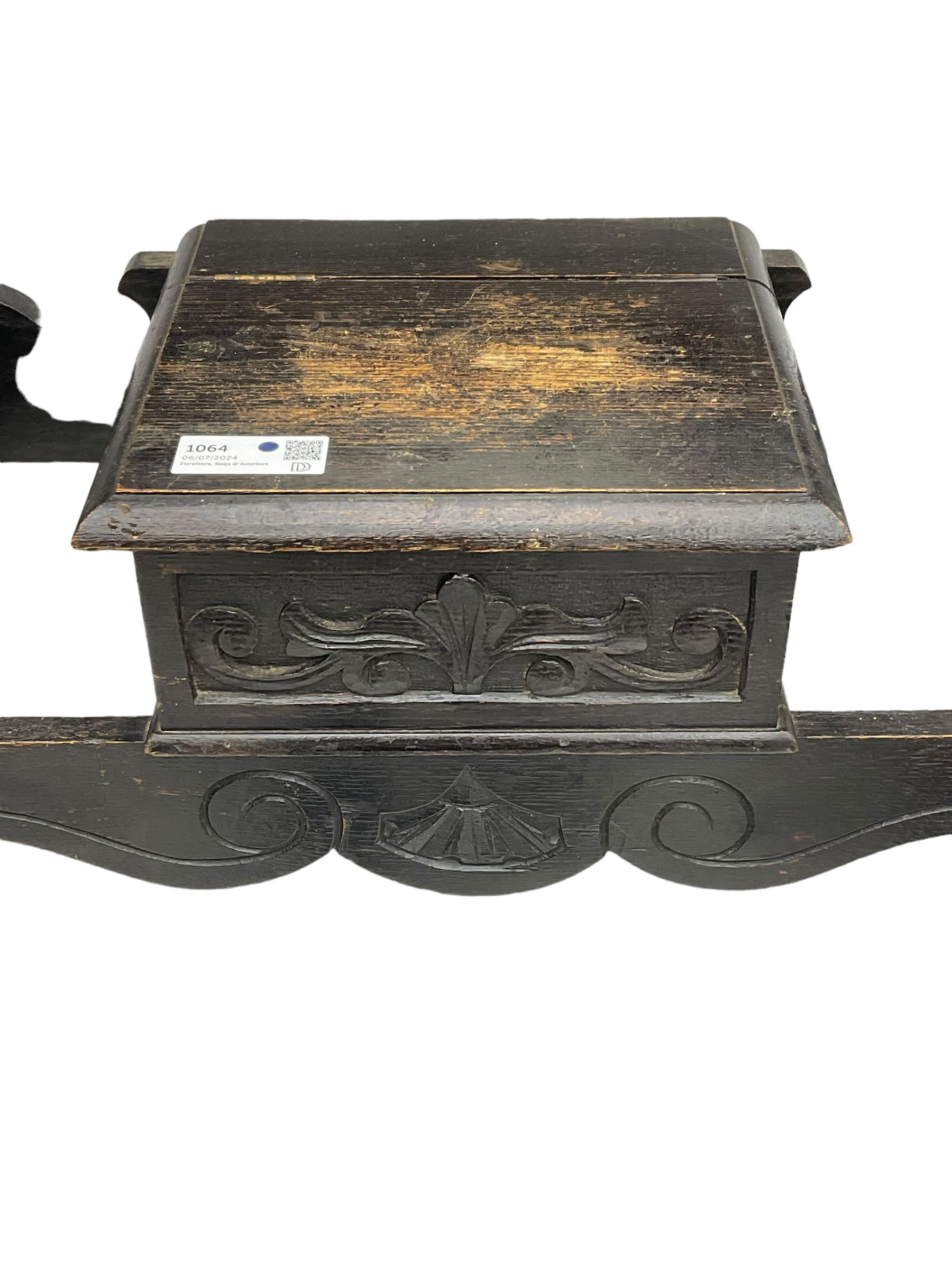 Victorian oak hall stand, the upper section featuring eight brass hooks and central mirror plate flanked by scroll-carved panels, the central section includes a storage box positioned above an umbrella stand, supported by square carved legs with scroll-carved horizontal supports