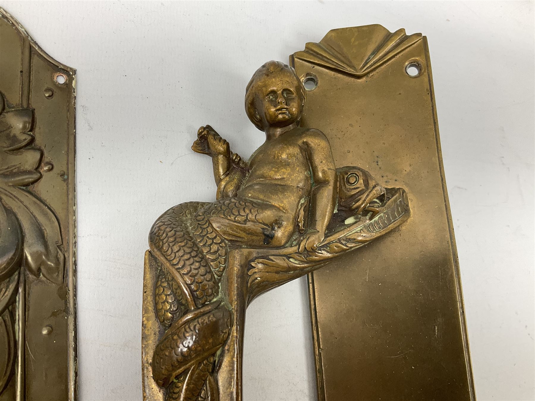 Art Nouveau bronze door handle modelled with a young merman holding a stylised fish, the plate decorated with geometric terminals, together with three repousse detail finger plates, largest L36cm