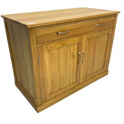 Contemporary light oak sideboard desk, rectangular top with full length drawer, hinged front panel revealing pull-out keyboard tray, over two panelled doors enclosing an assortment of shelves and compartments with cable management holes, on plinth base