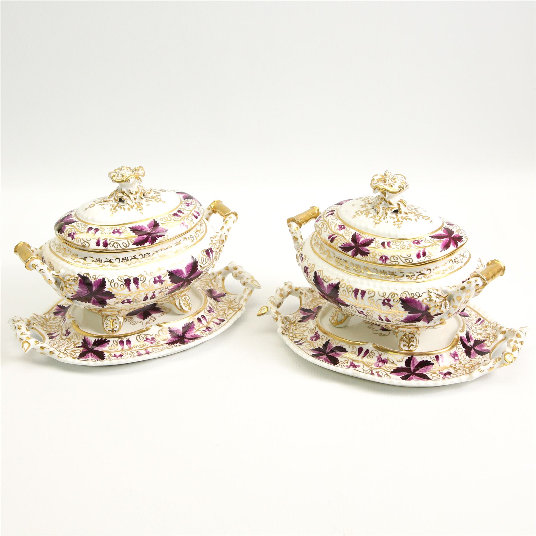 Pair of early 19th century porcelain sauce tureens and covers on stands, possibly Coalport, painted with bands of purple and gilt fruiting vines, within gadroon borders, the stands with naturalistic oak leaf and entwined moulded  handles, the covers with flower knop handles, stand L24cm, overall H18cm