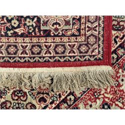 Persian Heriz design red ground carpet, the field decorated with a central star-shaped medallion surrounded by geometric floral motifs and angular vine patterns, the spandrels highlighted with palmette designs, the main border featuring a series of stylised rosettes and leaves against a dark blue ground, enclosed by multiple guard stripes with alternating floral and geometric motifs