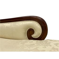 Regency design mahogany chaise longue, scrolled arms with carved rosette details, upholstered in cream damask fabric with bolster cushion, reeded frame supported by turned legs on brass castors