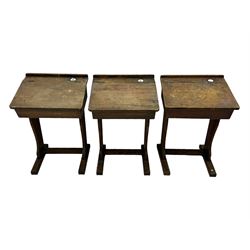 Three pitch pine school desks, each with rectangular lift-top with recessed ink well enclosing storage compartment, on trestle supports joined by stretcher