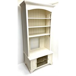 Cream painted bookcase on media stand, projecting cornice, three adjustable shelves above two glazed doors flanked by two cupboards, bracket supports 