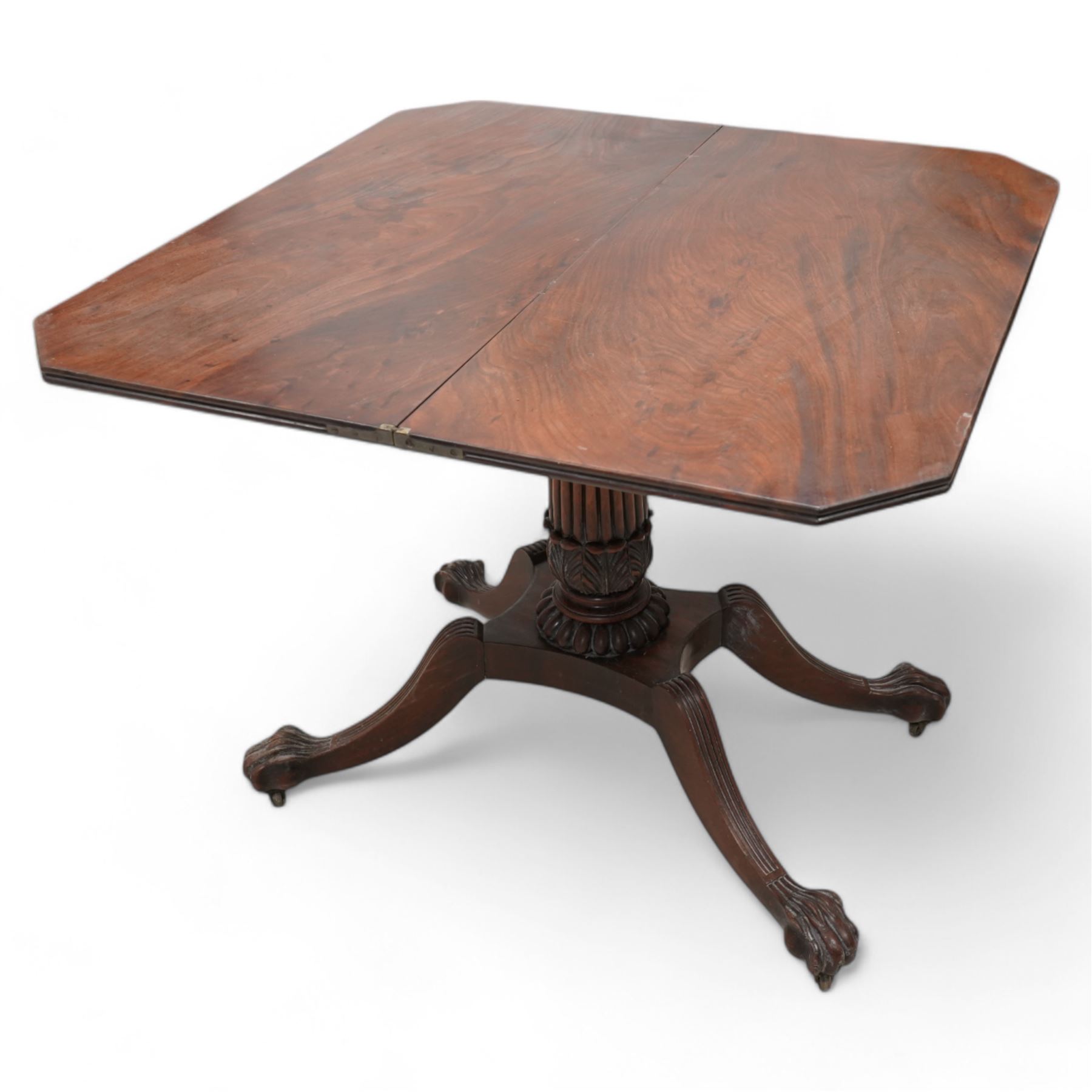 Regency mahogany card table, rectangular swivel and fold-over top with canted corners and reed-moulded edge, raised on a reeded pedestal with acanthus carved terminal and gardrooned collar, the concave rectangular base terminating to splayed supports with large paw feet on castors