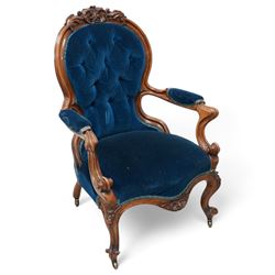 Victorian walnut framed open armchair, curled leaf carved cresting rail over scrolled and shaped arms, upholstered in buttoned blue velvet fabric, on cabriole feet