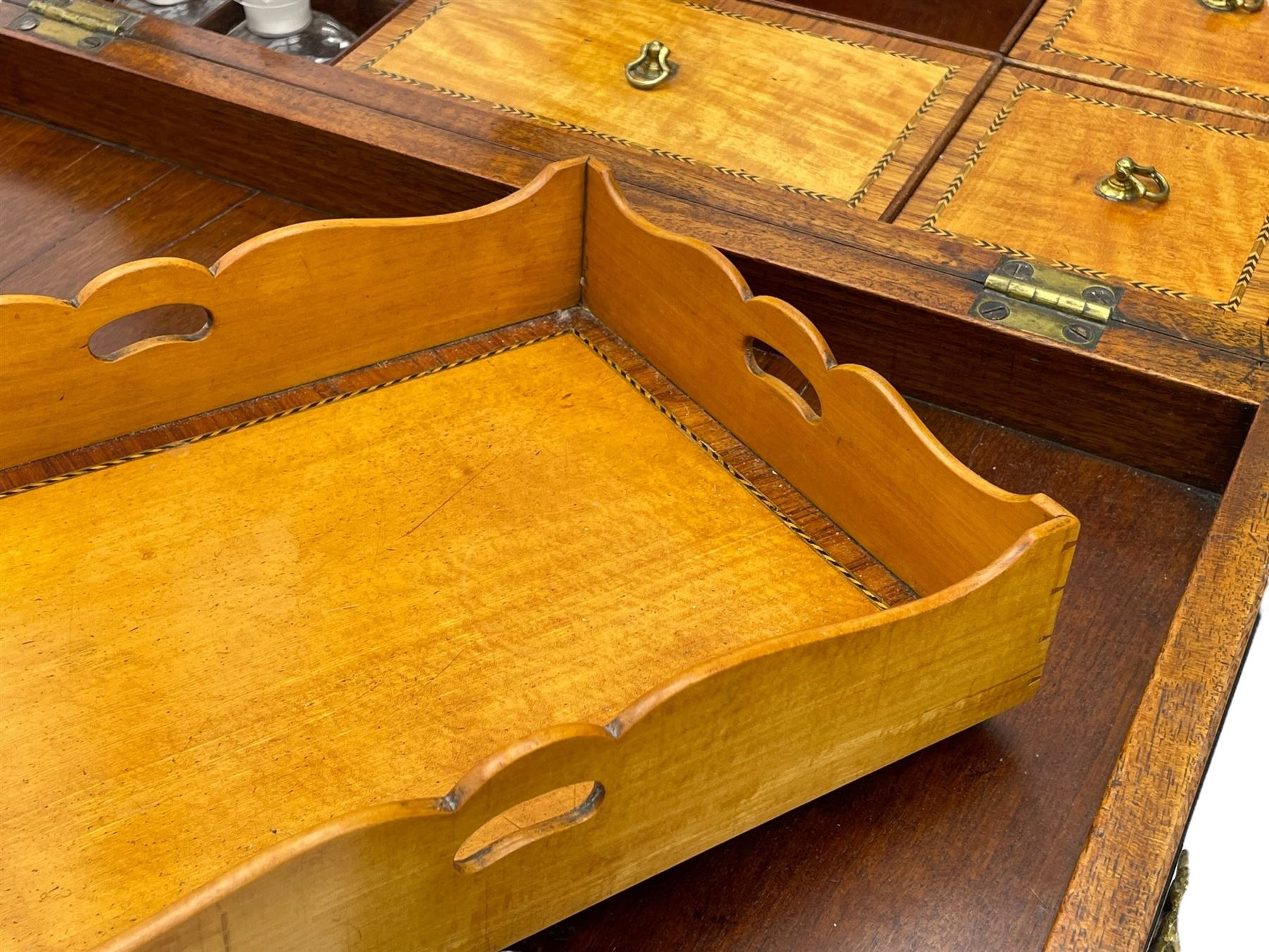 Late 19th century mahogany and satinwood dressing chest, the raised middle section hinges to reveal an interior fitted with lidded compartments, removable tray, single drawer and glass scent bottles, lift-up bevelled mirror with adjustable hinged mechanism, fitted with a further eight cock-beaded graduating drawers and curved kneehole with double cupboard, square tapering supports on brass cups and castors, inlaid throughout with checkered stringing, ornate Rococo cast gilt metal handles