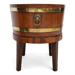 George III Chippendale design brass bound mahogany wine cooler of oval form, the coopered body enclosed by two brass brands, with lead liner to interior, fitted with twin lion mask ring handles, raised on square tapering supports