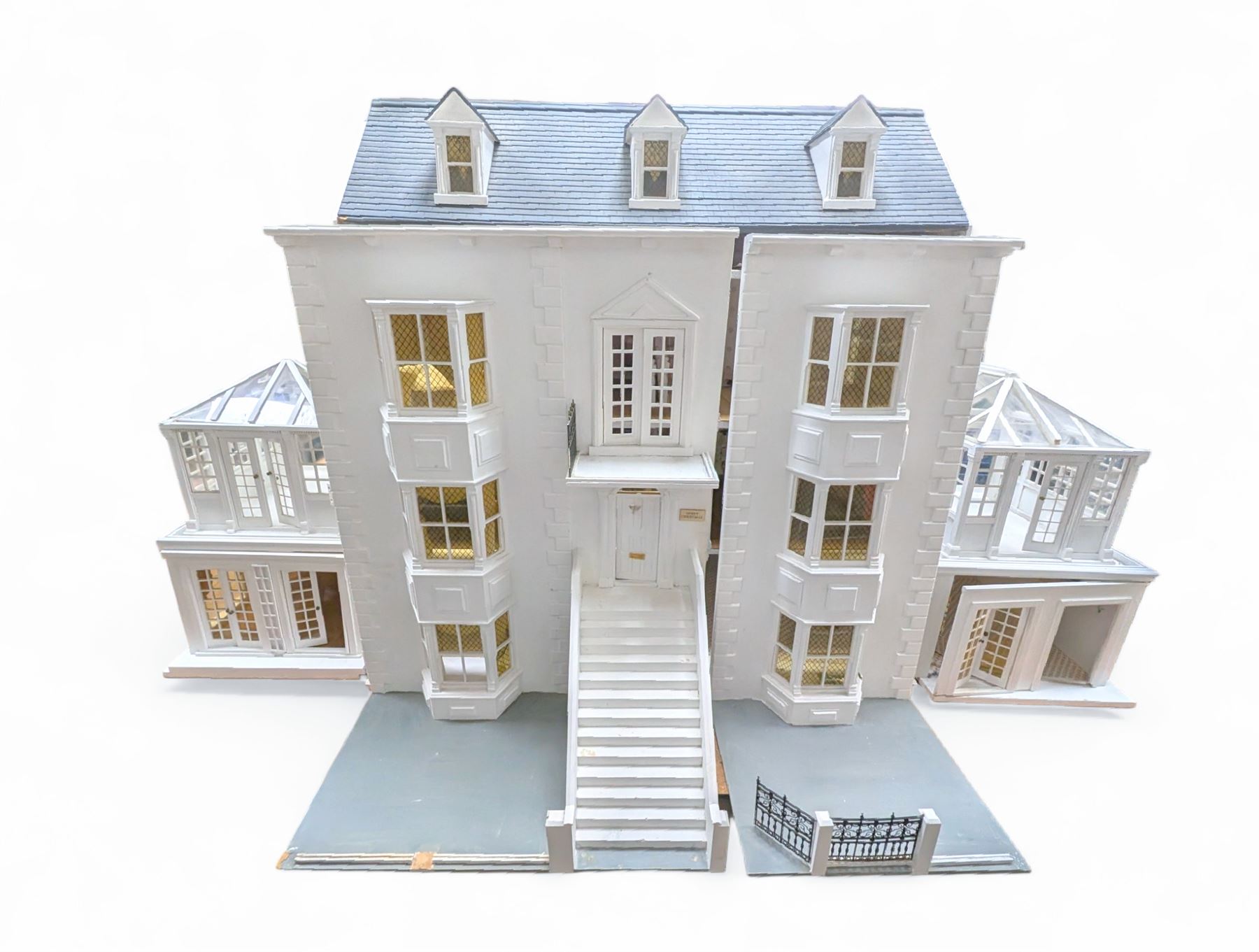 Large three storey modern dolls house, painted white with latticed windows, grey roof and metal fencing, with decorated interior, together with two dolls house garden rooms and two conservatories