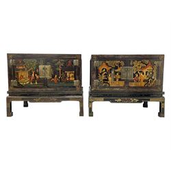 Pair of early 20th century Chinese ebonised and lacquered wood cabinets, the top decorated with dragons over lapping waves within a gilt patterned panel, the surrounding band decorated with Chinese symbols and flowerheads, enclosed by two doors each with village scenes with pagodas, figures and trees, the panelled sides decorated with a figure riding a dragon on stands with gilt decorated 