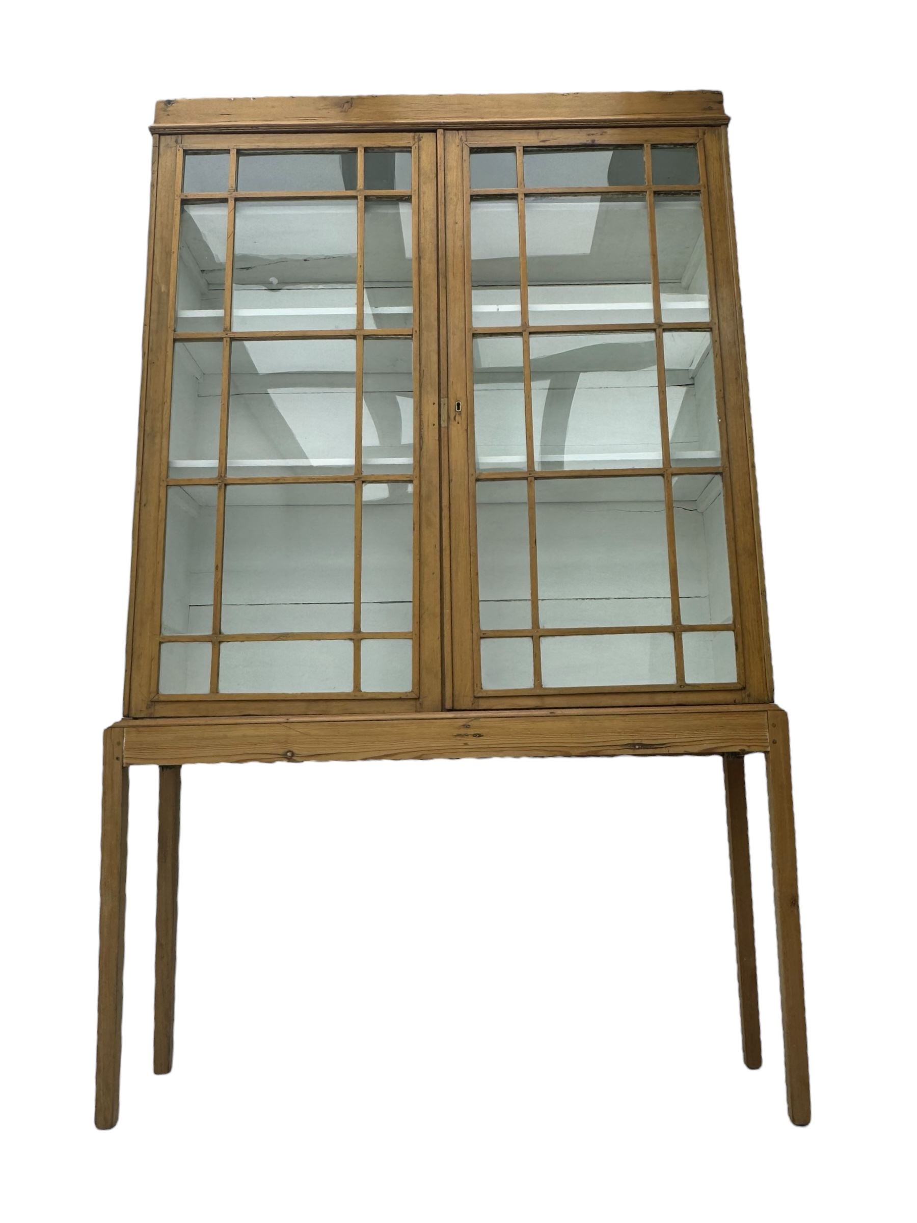 Georgian stripped pine bookcase display cabinet, plain moulded cornice over two glass-panel doors with multiple panes, enclosing white painted interior with three shelves, raised on square supports