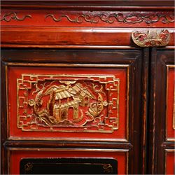 19th century Chinese red and black lacquered hardwood cabinet fitted with four panelled doors, the frieze decorated with scrolling gilt patterns over gold bat mounts surmounting the hinges, the black panels depicting traditional figural and floral scenes, the carved parcel-gilt panels with pagoda, pastoral and war scenes, the doors fitted with metal fish and pagoda handles, enclosing a single shelf and four internal drawers, the base compartment decorated with carved precious objects, raised on moulded square supports with pierced scrolling brackets