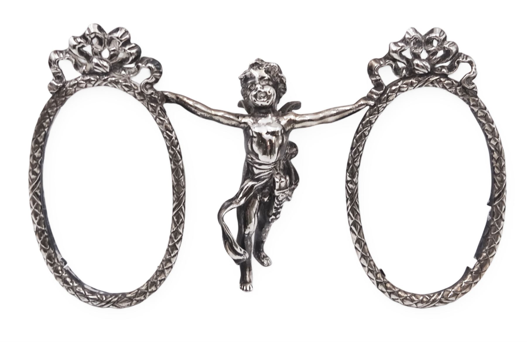 Edwardian silver double photograph frame by Berthold Herrman Muller, the oval frames each with ribbon surmount and supported by a central cherub, H8.5cm