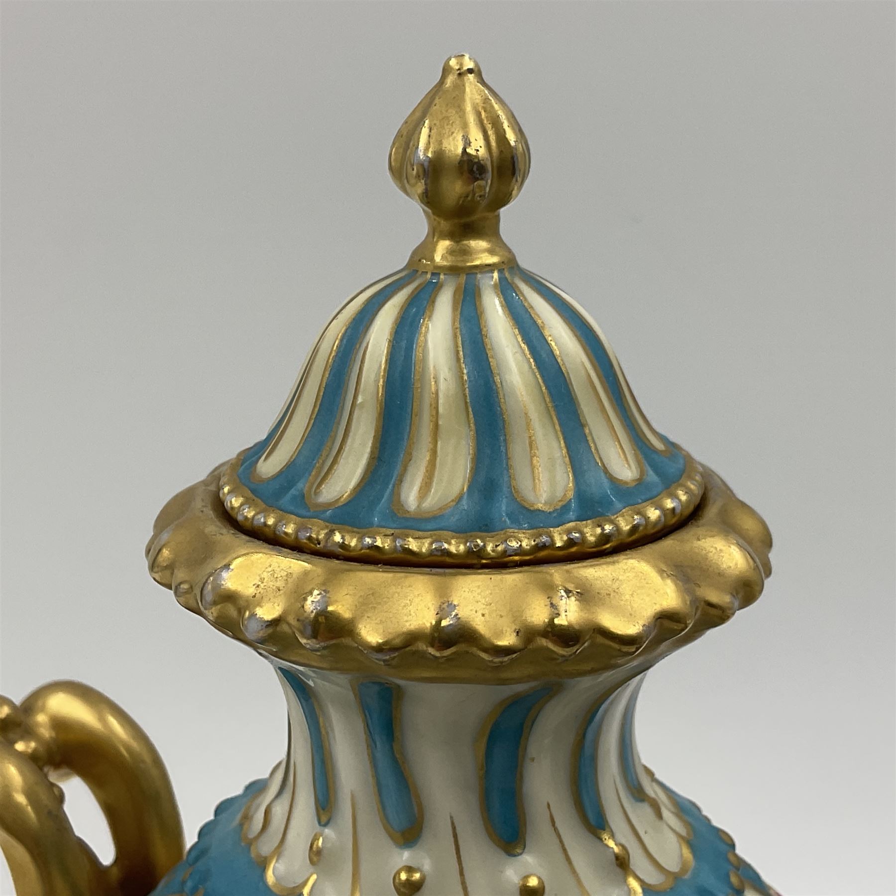 Pair of late 19th/early 20th century Sevres style vases and covers, of baluster form with gilt scroll handles and domed covers, the wrythen fluted bodies decorated with alternating bands of painted fruit and flowers and gilt vines, upon a white and celeste blue ground, with printed and impressed marks beneath, H22.5cm 