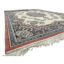 Persian design ivory ground rug, the field decorated with an oval medallion filled with floral motifs and scrolling vines, flanked by floral sprays and corner spandrels with palmette designs, the main border featuring a series of stylised floral patterns against a dark blue ground, enclosed by multiple guard stripes with geometric and floral motifs