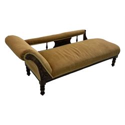 Late 19th century mahogany framed chaise longue, upholstered in tan fabric, featuring scrolled backrest with carved floral motifs, supported by turned legs