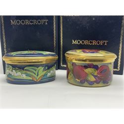 Two Moorcroft enamel boxes, the first example of oval form, decorated with lily of the valley upon a blue ground, the second of circular form, decorated in pomegranate pattern, each with fitted box  