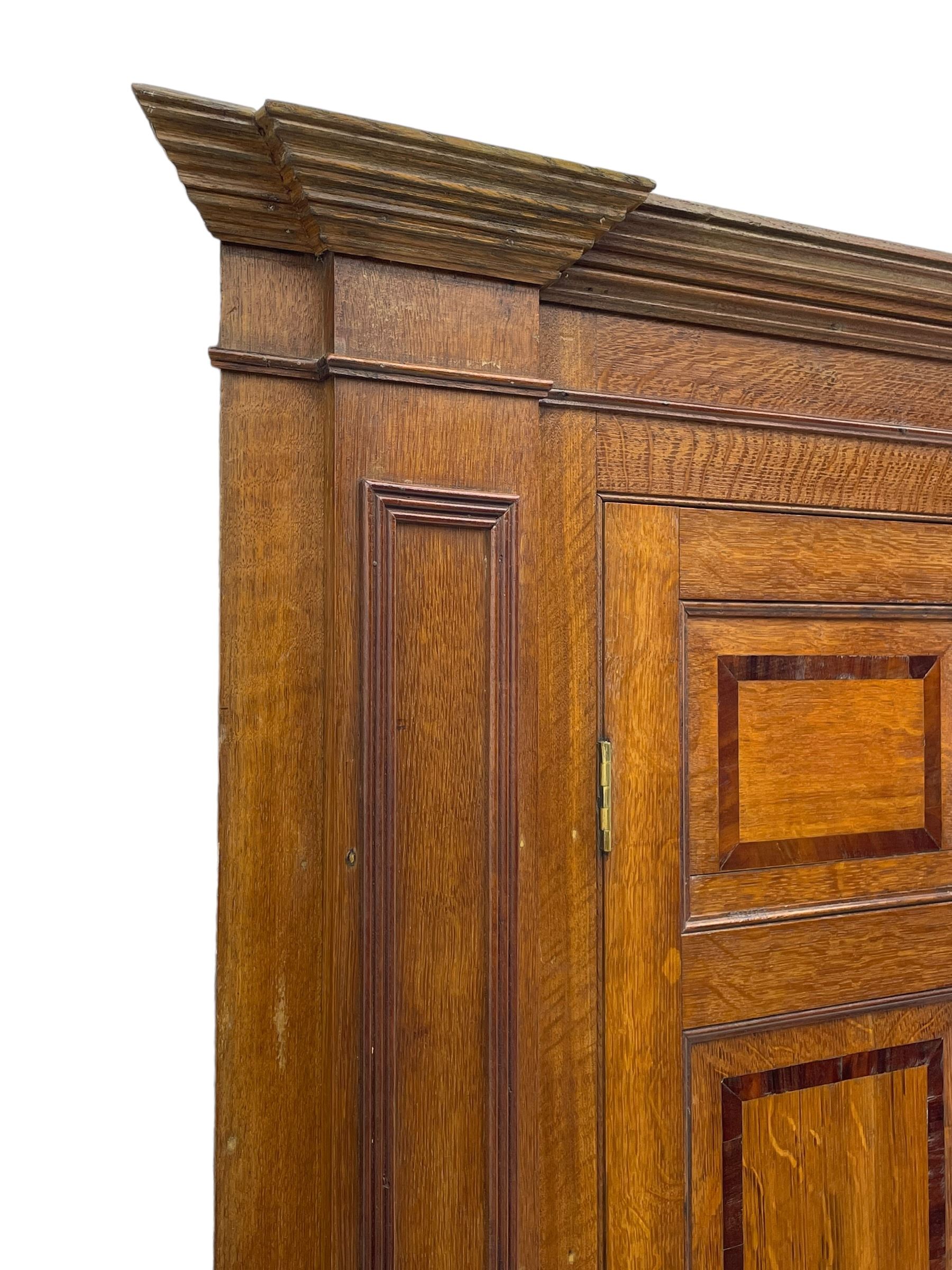 George III and later oak and mahogany banded corner cupboard, moulded cornice over four panelled doors, the door panels inlaid with mahogany bands, projecting square pilasters throughout with applied reeded mouldings, the painted interior fitted with shaped shelves, on moulded plinth base 