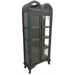 Tall painted glazed display cabinet, double arched top over two glazed doors, fitted with three shelves, in rustic blue paint finish, on cabriole feet