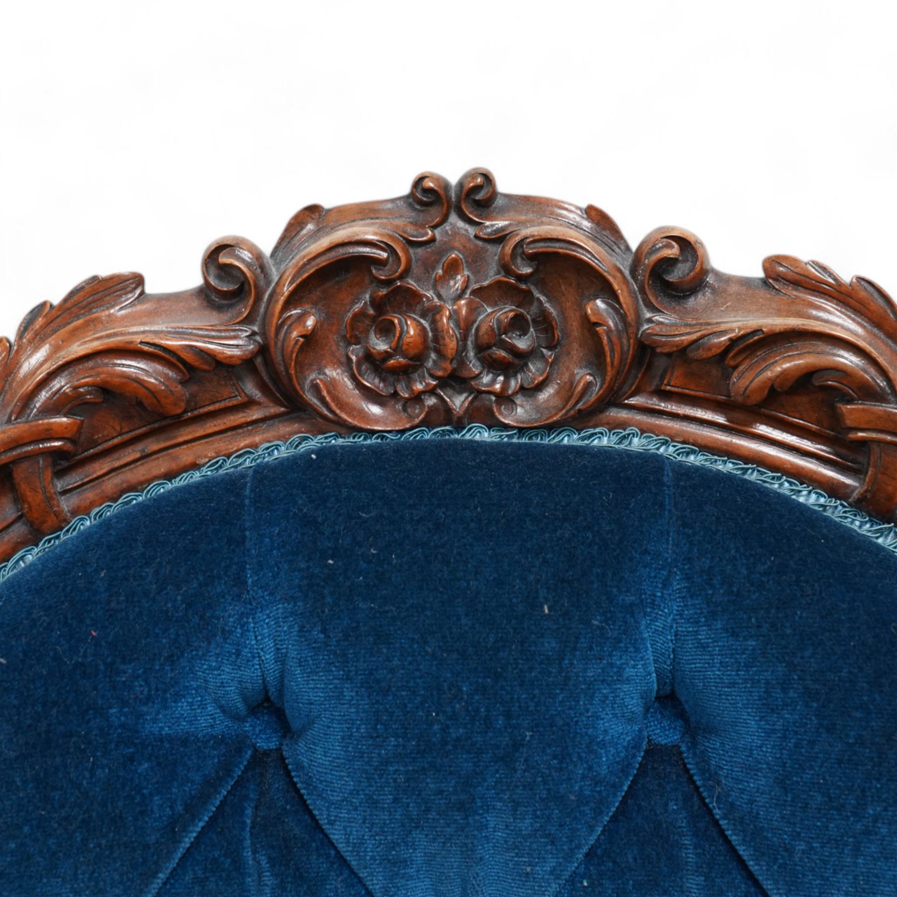 Victorian walnut framed open armchair, curled leaf carved cresting rail over scrolled and shaped arms, upholstered in buttoned blue velvet fabric, on cabriole feet