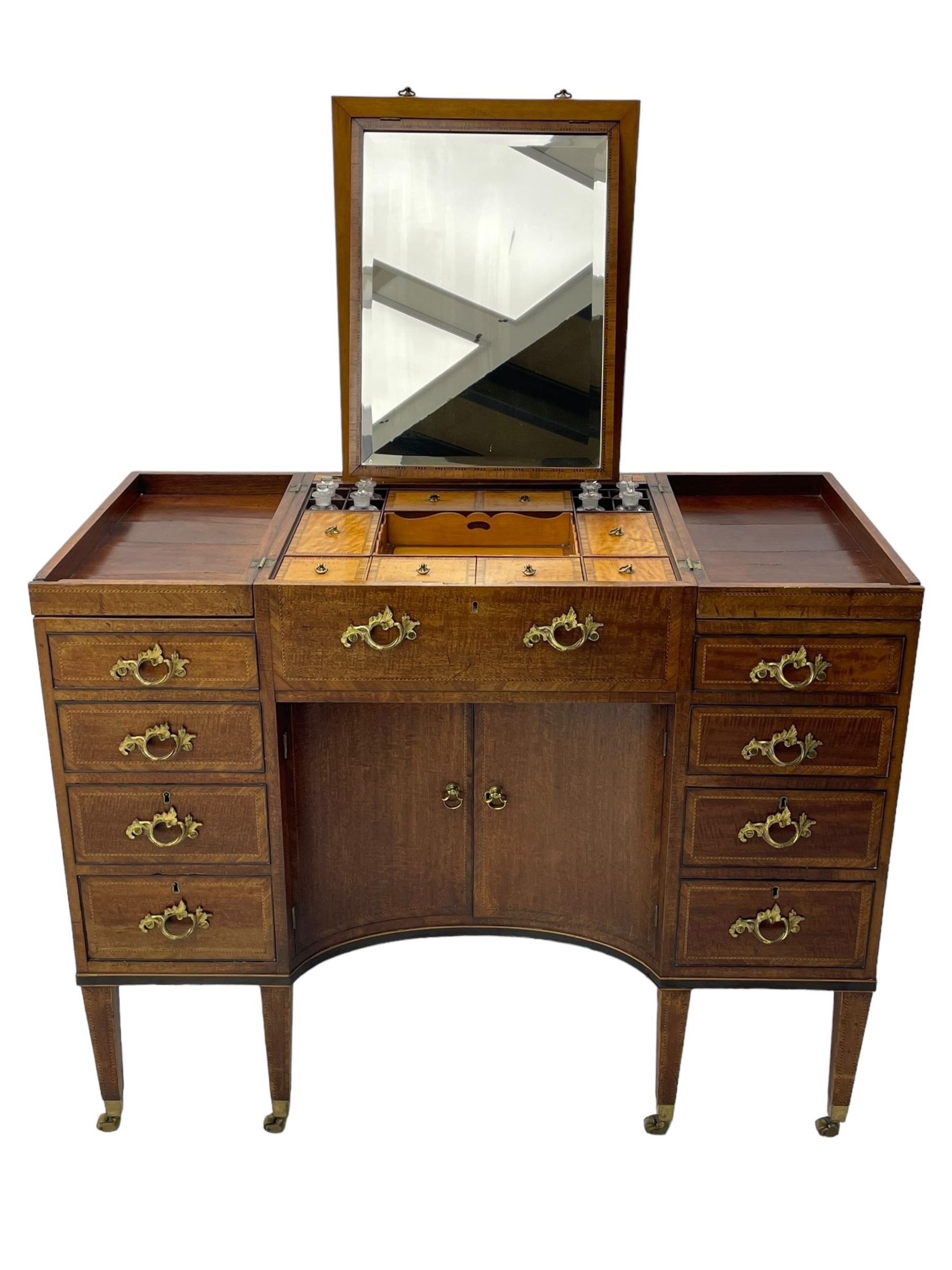 Late 19th century mahogany and satinwood dressing chest, the raised middle section hinges to reveal an interior fitted with lidded compartments, removable tray, single drawer and glass scent bottles, lift-up bevelled mirror with adjustable hinged mechanism, fitted with a further eight cock-beaded graduating drawers and curved kneehole with double cupboard, square tapering supports on brass cups and castors, inlaid throughout with checkered stringing, ornate Rococo cast gilt metal handles