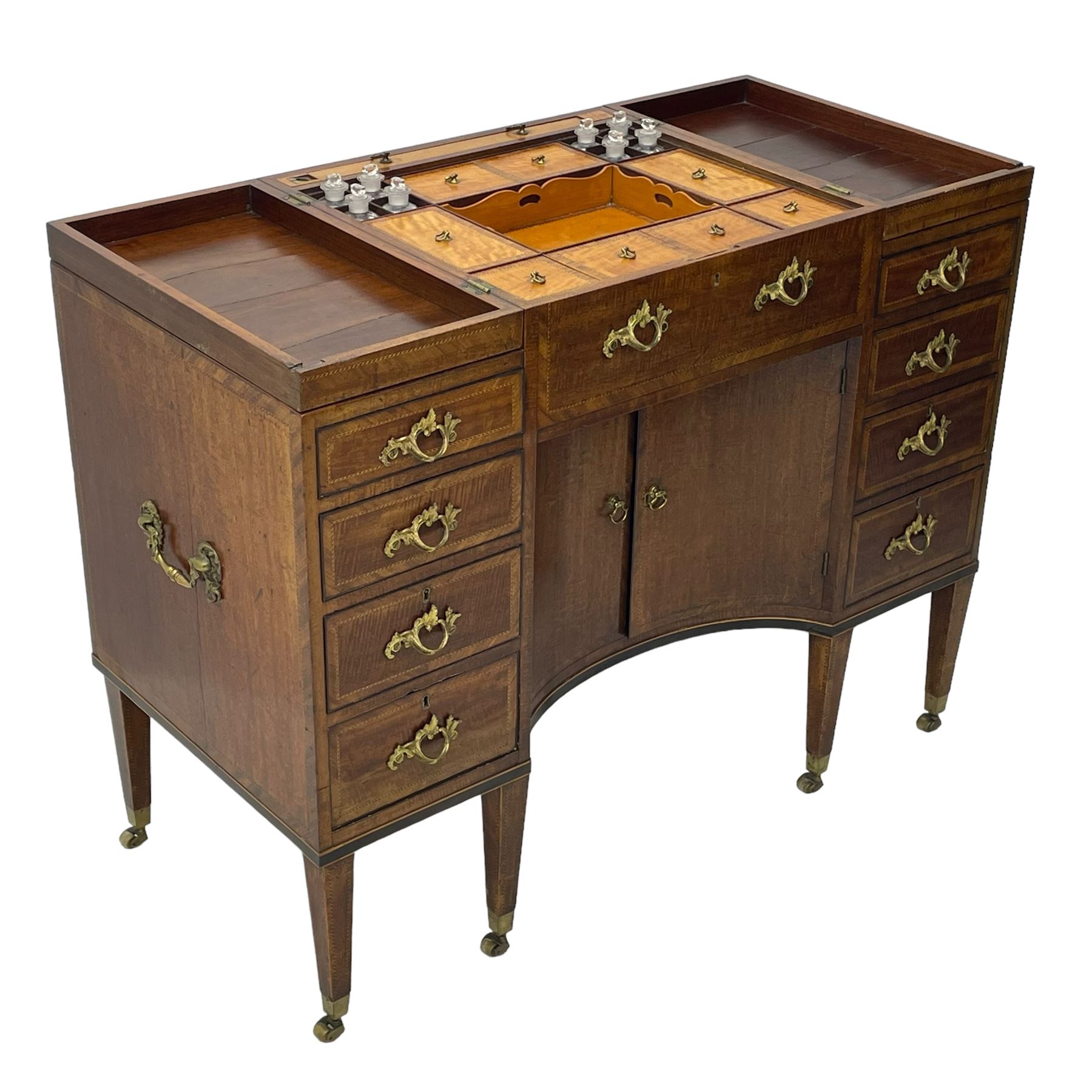 Late 19th century mahogany and satinwood dressing chest, the raised middle section hinges to reveal an interior fitted with lidded compartments, removable tray, single drawer and glass scent bottles, lift-up bevelled mirror with adjustable hinged mechanism, fitted with a further eight cock-beaded graduating drawers and curved kneehole with double cupboard, square tapering supports on brass cups and castors, inlaid throughout with checkered stringing, ornate Rococo cast gilt metal handles