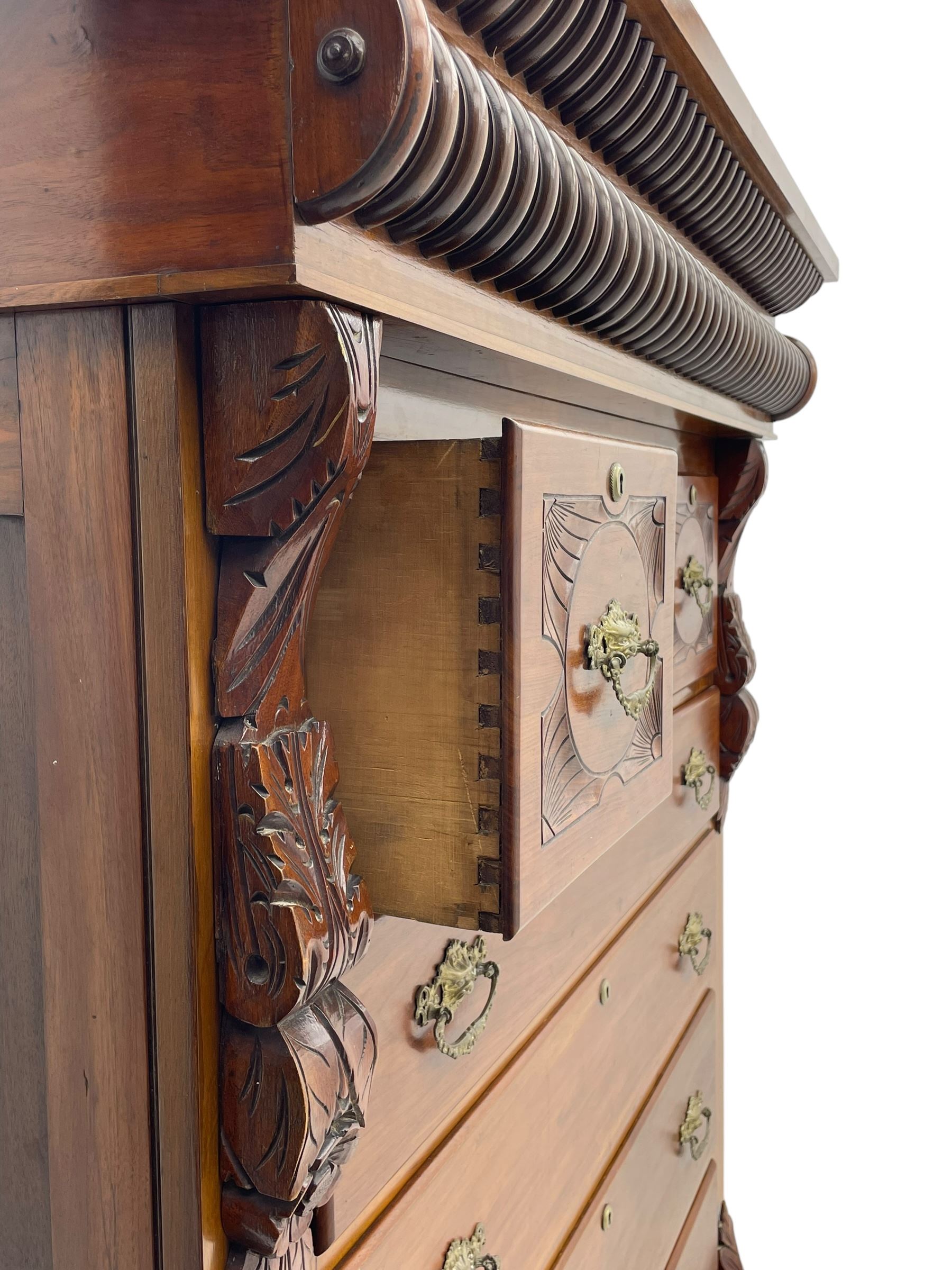 Late Victorian walnut Scotch chest, projecting cornice with turned quarter column mounts over matching half column to frieze, fitted with two upper short drawers with central cupboard, bevelled mirror glazed cupboard door, four graduating drawers below, foliage and flower head carved brackets to the uprights, panelled sides, chamfered plinth on turned feet