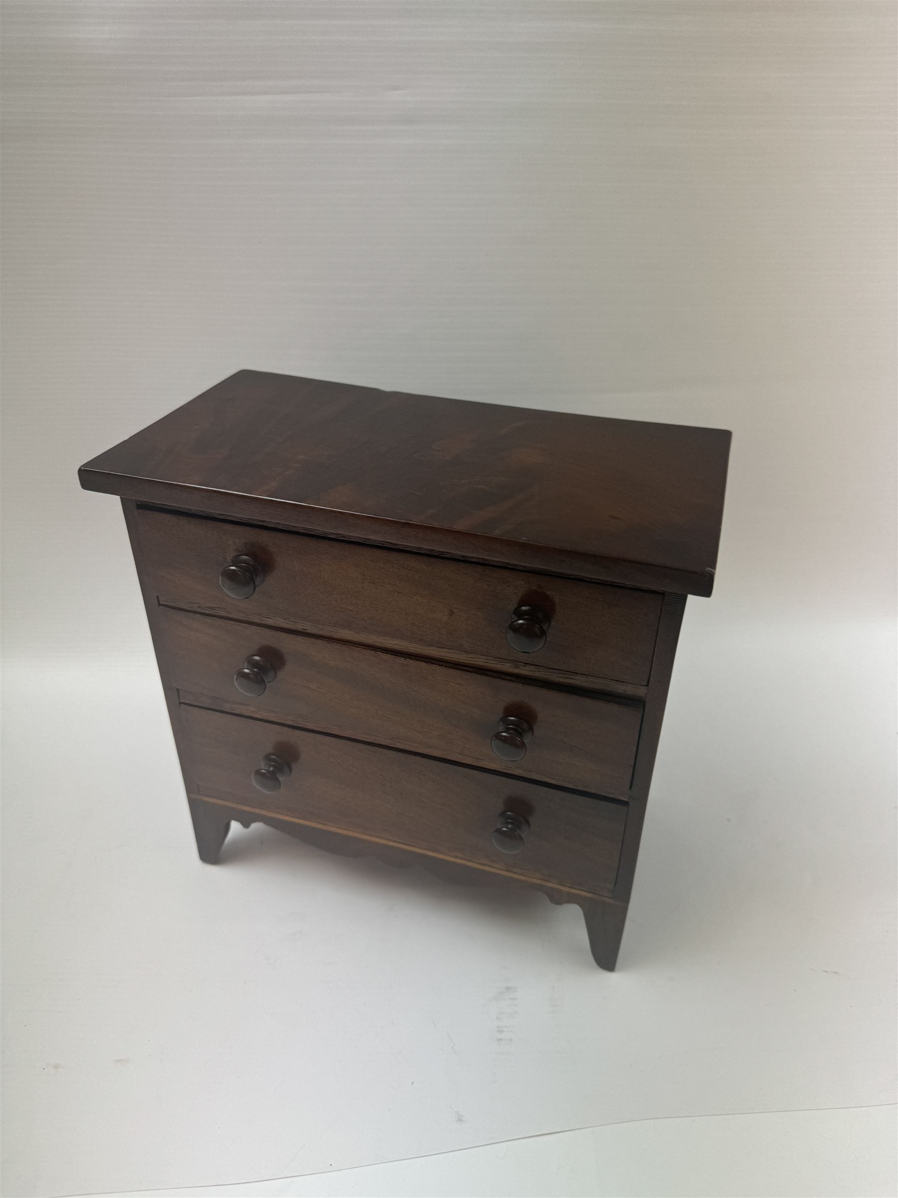 19th century mahogany miniature chest of drawers, with three graduating drawers, each with wooden handles, with inlaid shaped front and upon four bracket feet, H24cm