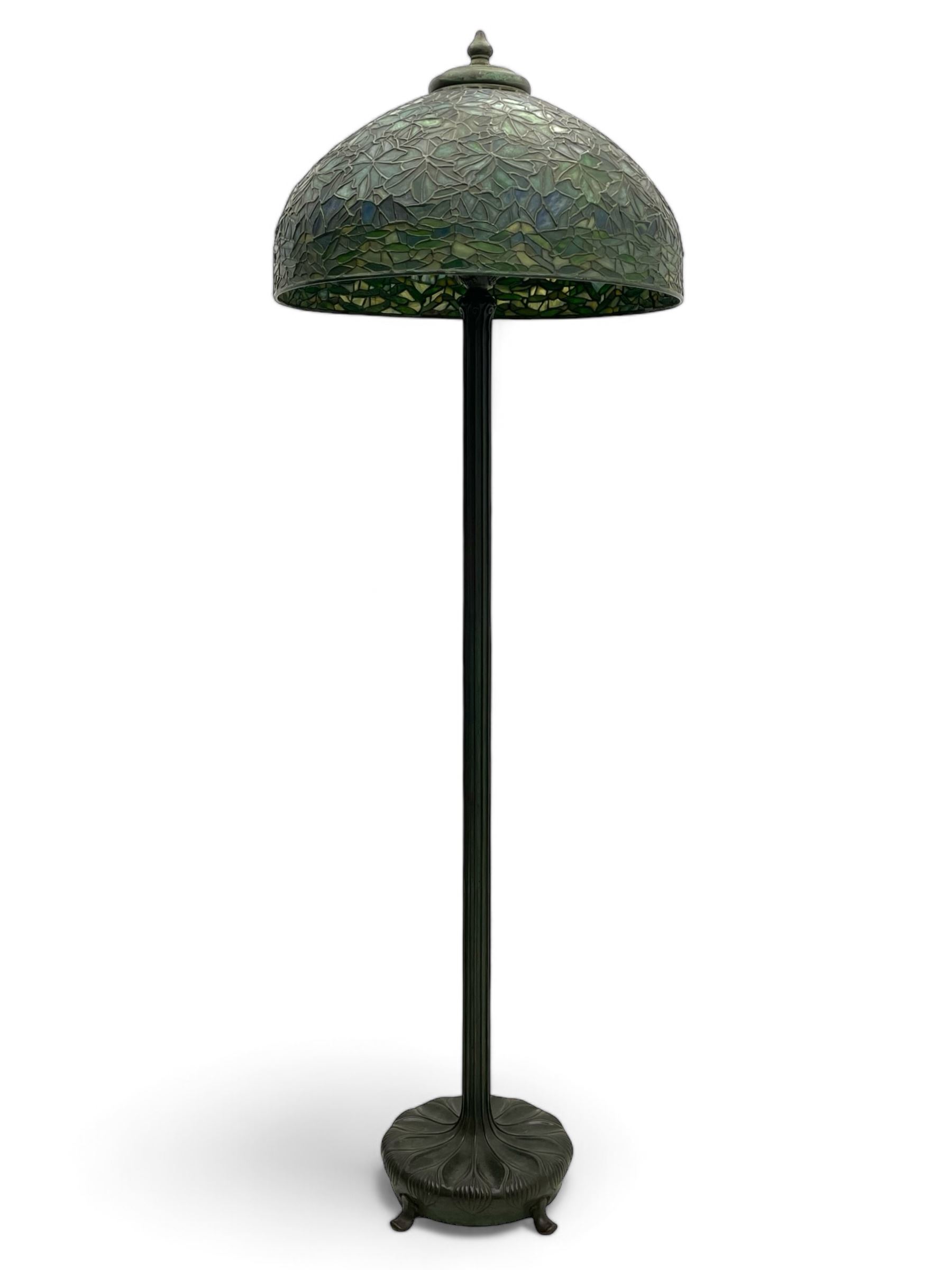 In the manner of Tiffany & Co. - bronze 'Chased Pod' design floor lamp, 'Maple Leaf' dome leaded glass shade decorated with flowers in blue and green shades, six branches on column decorated with stylised trailing stems terminating to circular base with stylised plant decoration, on scrolled feet, the base stamped 'Tiffany Studios New York 379' the inner shade stamped 'Tiffany Studios New York [...]'