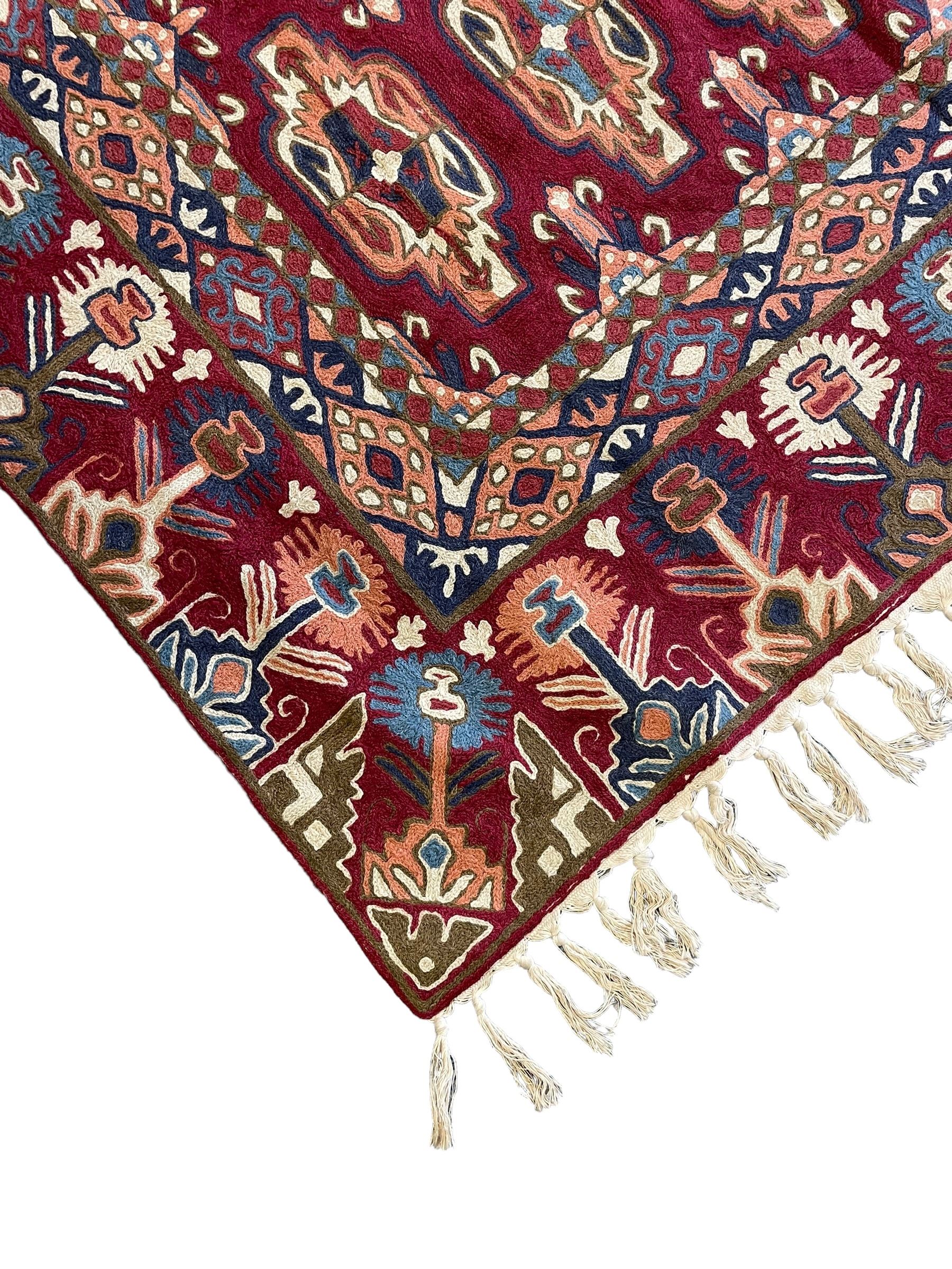 Caucasian design crewelwork hanging, crimson ground, the field decorated with geometric designs, the wide guard band with repeating stylised plant  motifs