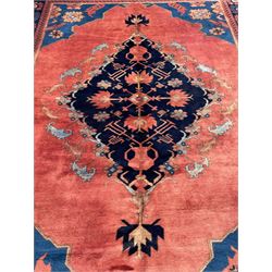 Afghan rust ground carpet, large central lozenge medallion decorated with stylised plant motifs, running water guard stripes enclosing indigo ground border decorated with stylised flower heads